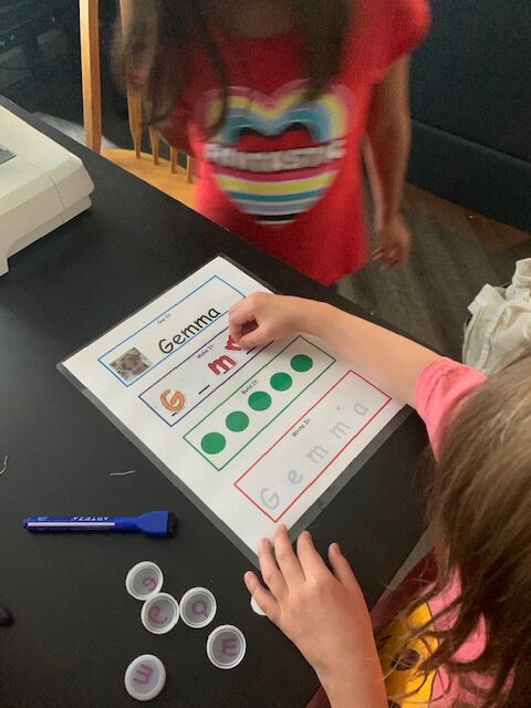 Gemma writes the letters in her name. She places stickers on the second line in red.