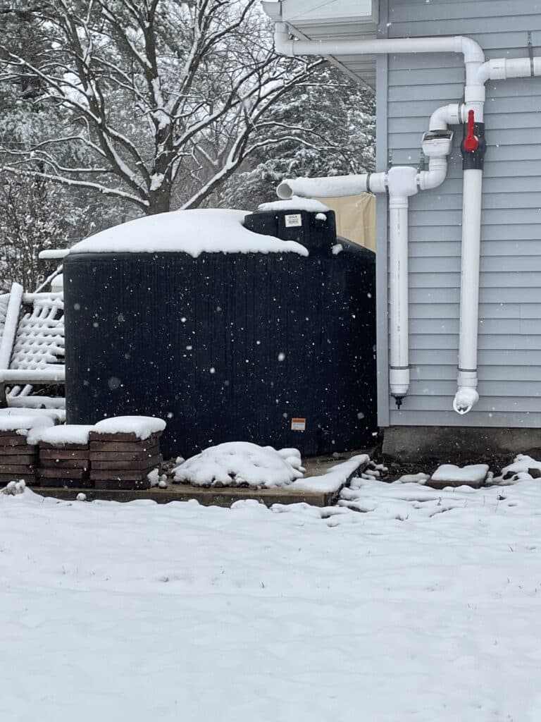 Large black water storage box just outside house with snow cover.